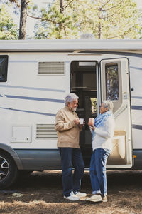 Senior couple with coffee cup standing by motor home in forest