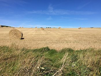 Hay bales on field against cloudy sky