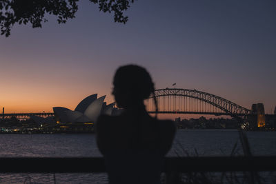 Rear view of silhouette woman with suspension bridge in background