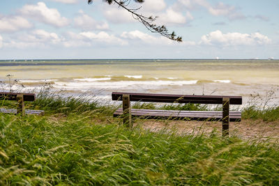 Empty bench on field by sea against sky