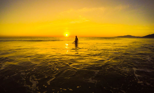 Rear view of woman standing at beach against sky during sunset