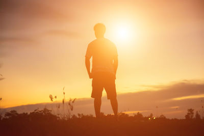 Rear view of silhouette man standing on field against sky during sunset