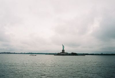 Statue in sea against cloudy sky