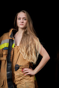 Portrait of young firefighter standing against black background