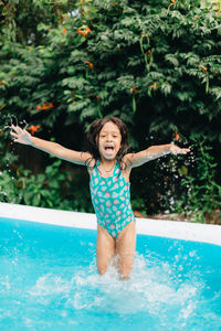 Diverse mixed race toddler girl at home having fun in kiddie pool in backyard being very happy