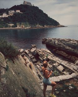 Rear view of woman standing on cliff by sea against sky