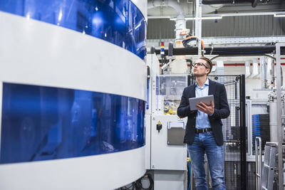 Man holding tablet looking at machine in factory shop floor