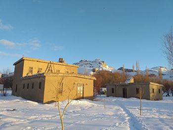 Snow covered field by buildings against sky