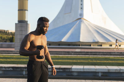 Full length of shirtless man standing against sky in city