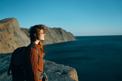 Man standing on rock by sea against clear sky