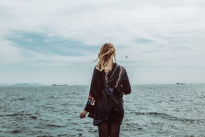 Rear view of woman standing at beach against sky