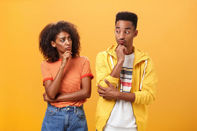 Young couple standing against yellow background