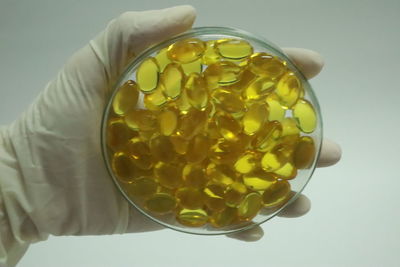 Close-up of hand holding yellow glass over white background