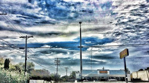 Low angle view of electricity pylon against cloudy sky