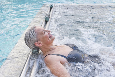 Senior white woman enjoying water massage. hydromassage in outdoor thermal swimming pool. 