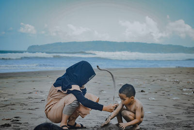 Rear view of boys playing on beach against sky