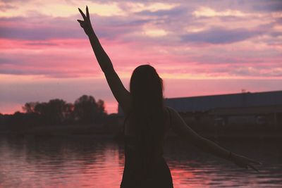 Silhouette woman standing at lakeshore against sky during sunset