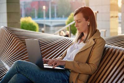 Woman sitting with a laptop on steps outdoors against sunset.