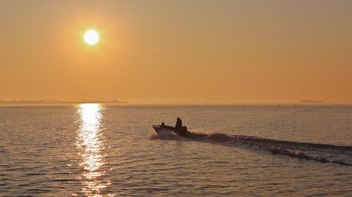 Silhouette man rowing boat in sea against sky during sunset