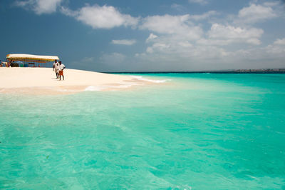 Men at beach in turquoise sea against sky