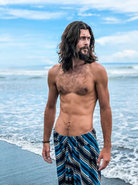 Young man standing at beach against sky