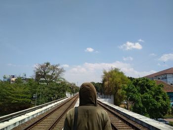 Rear view of man on railroad tracks against sky