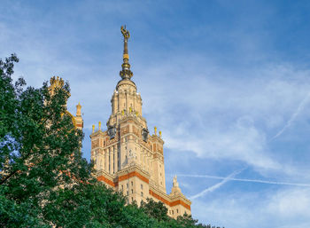 Bottom up view of moscow university building, green tree branches and blue cloudy sky