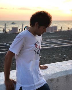 Man standing at beach against sky during sunset