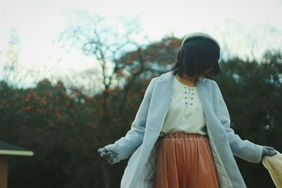 Woman with tousled short hair standing against plants during winter