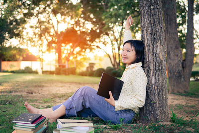 Young woman sitting on book against tree trunk