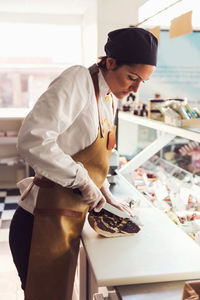 Side view of female owner cutting meat at counter in grocery store