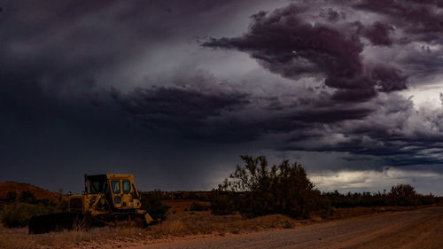 Built structure on field by road against storm clouds