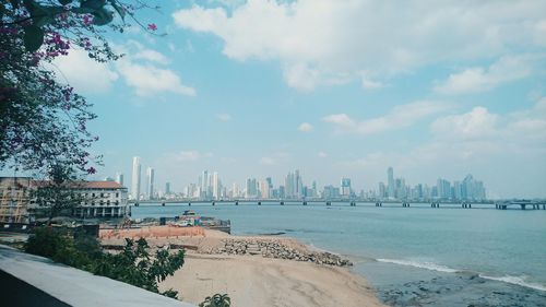 Distant view of city by sea against sky