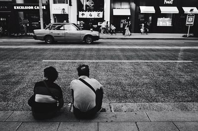 Rear view of people sitting on sidewalk