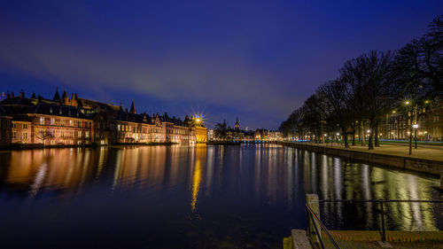 Illuminated buildings by lake against sky at night