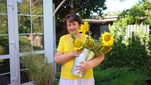 Portrait of smiling woman standing by yellow flowering plants