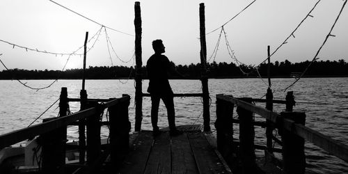 Rear view of silhouette man fishing on pier against sky