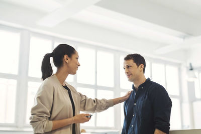 Young businesswoman with hand on male colleague's shoulder in office