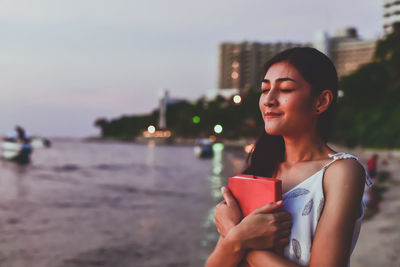 Young woman holding book at beach in city