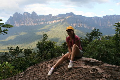 Man sitting on mountain against sky