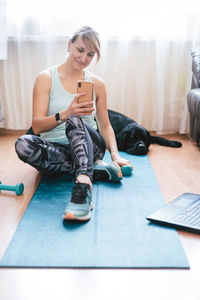 Woman with smart phone sitting on exercise mat