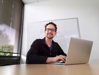 Portrait of businessman using laptop at table in office