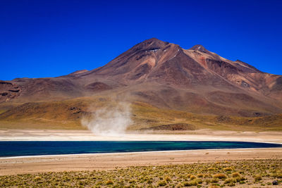 Scenic view of arid landscape with salt lake and sand storm against clear blue sky - atacama desert