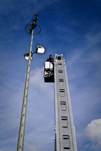 Low angle view of man on cherry picker by street light against sky