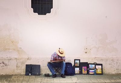 Man sitting on seat against wall