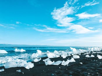 Scenic view of icebergs at beach against blue sky
