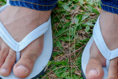Close-up low section of man wearing flip-flop on grass