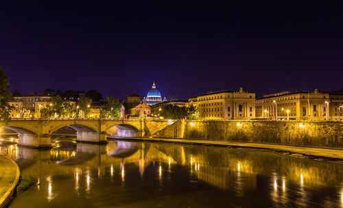 Illuminated bridge over river against buildings at night