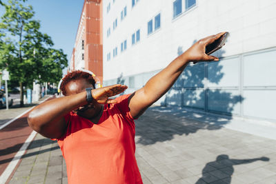 Woman holding smart phone doing dab on sunny day