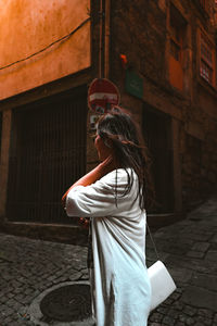 Midsection of woman standing on footpath by street against building